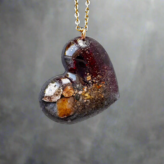 Heart-shaped pendant with embedded stones on a gold chain against a gray background