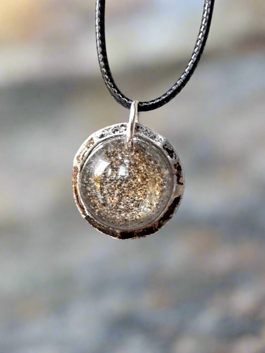 Silver pendant with a textured surface on a black cord against a light gray background