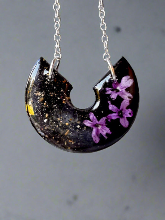 Necklace with a crescent-shaped pendant featuring purple flowers on a light gray background
